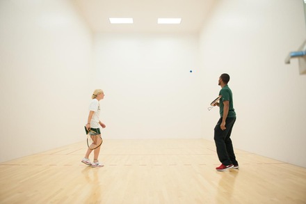 Two students playing racquetball. Male student preparing to hit/return ball to female student.