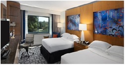 Photo of Hilton hotel room with two beds with a lamp in between, a television and chair.