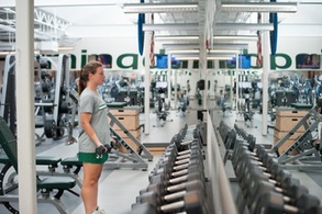 Female student lifting dumbbell weights in weight room.