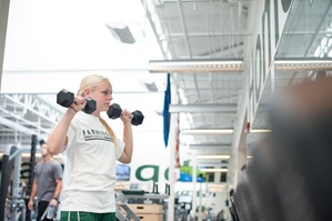 Female student-athlete lifting free weights inside weight room.
