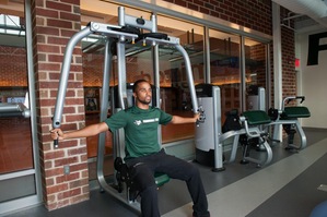 Male student-athlete using chest fly machine in weight room.